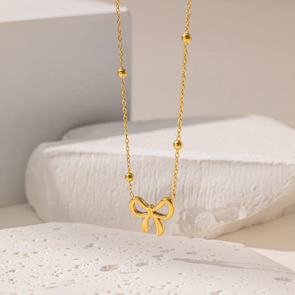 Gold electroplated bow necklace with adjustable chain on dark background