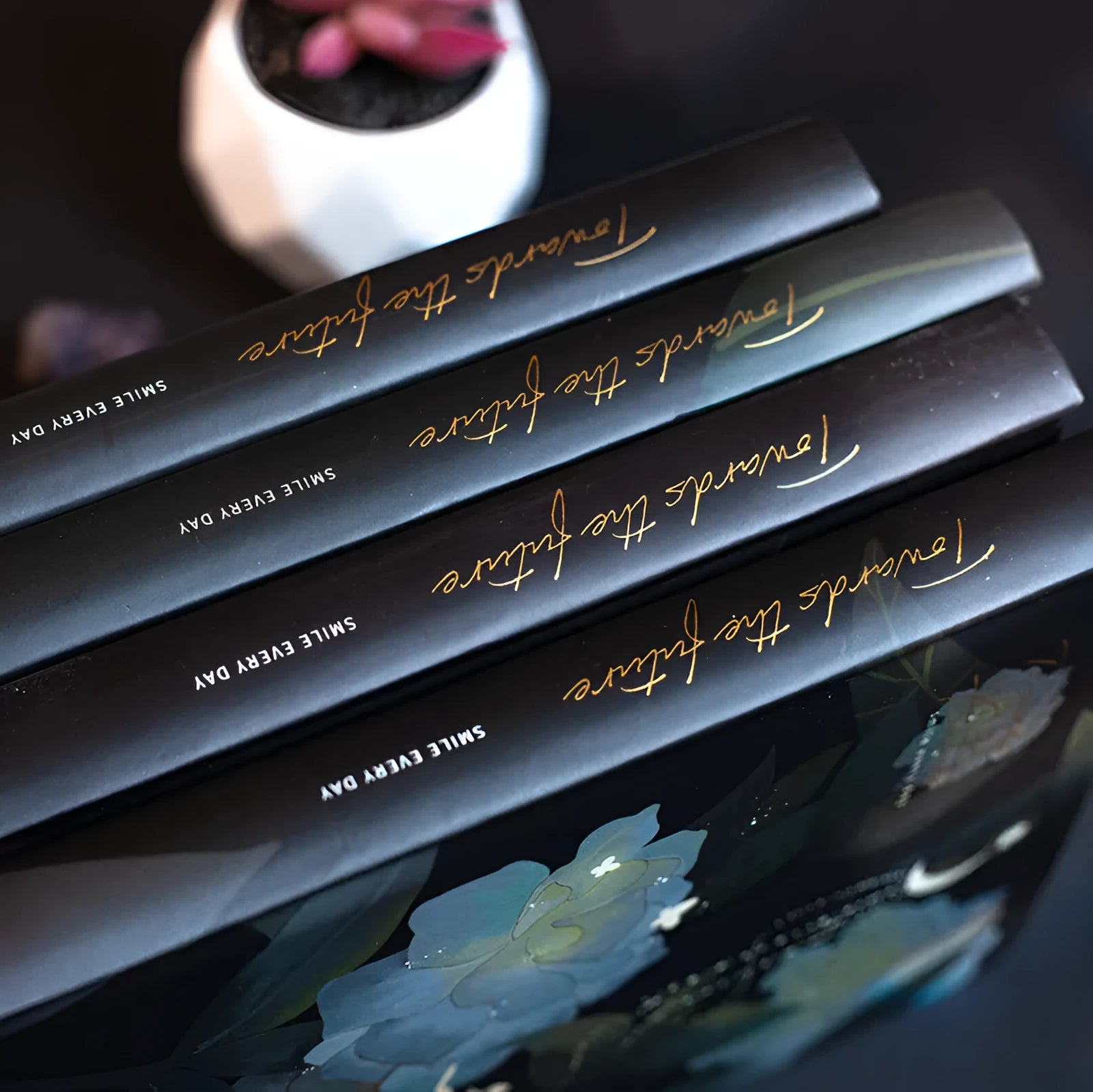 A5 notebook with a luminous cover open to show internal colour illustrations, next to Purple, Light Blue, Gold, and Deep Blue colour options.