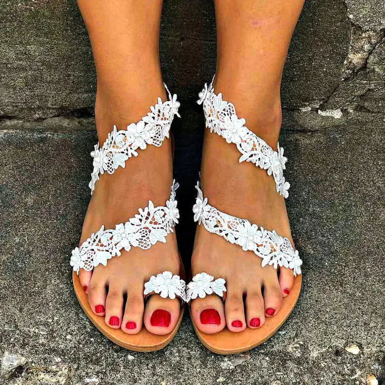 White women's flat sandals with rhinestone flower decoration on PU upper and rubber sole.