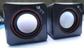 Black square USB computer speaker on desktop next to monitor