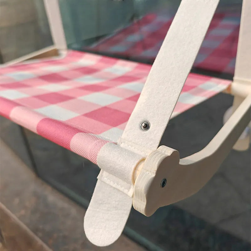 Pink wooden cat hammock with suction cups attached to a window, showing a cat resting on the linen fabric.