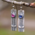 A pair of antique finish red sapphire earrings with a geometric shape and oval details on a white background.
