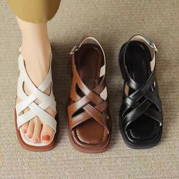 Women's glossy patent leather square-toe sandals with cross-strap fastening on a neutral background