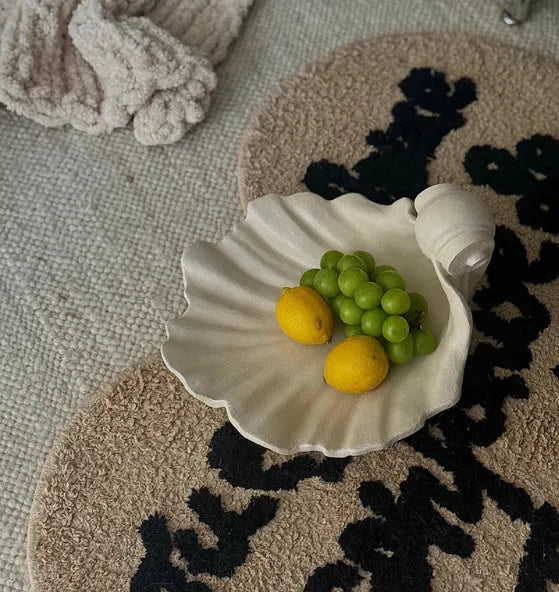 White resin shell-shaped fruit plate ornament on a table.