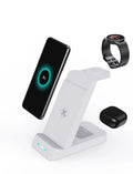 Black or white 3-in-1 wireless charging stand for phone, smartwatch and AirPods on a desk.
